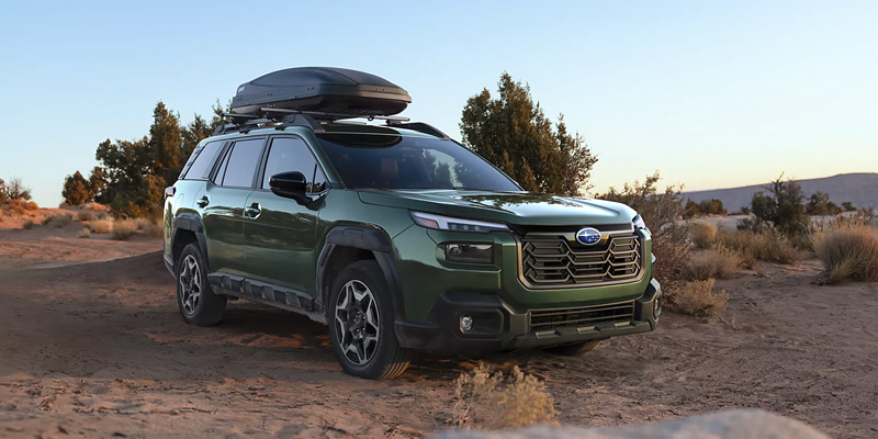 A green Subaru SUV parked on a dirt road with a rooftop cargo carrier