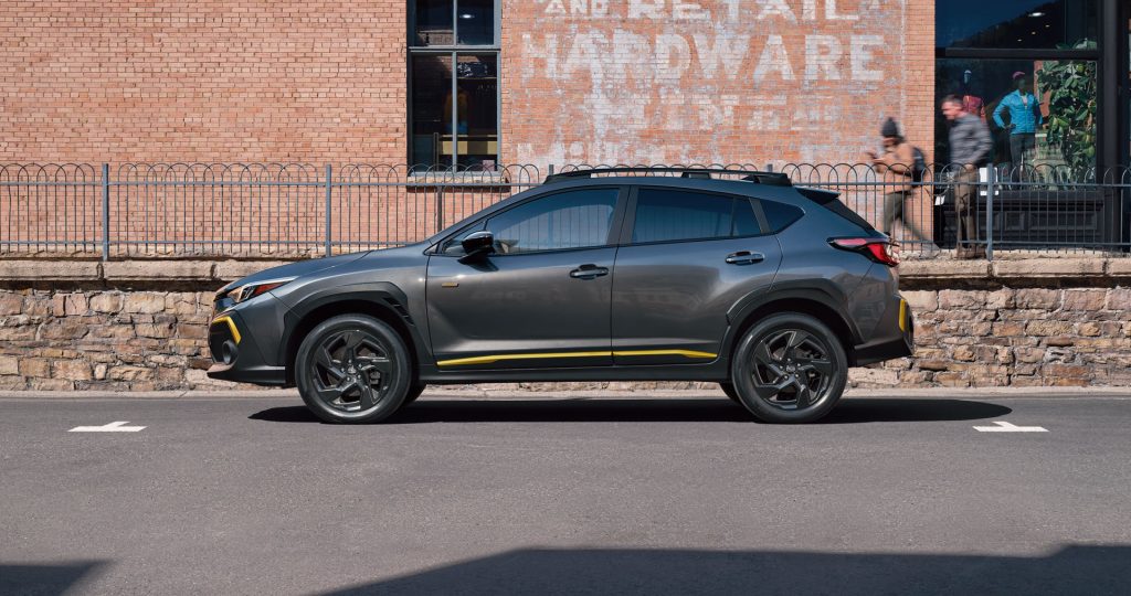 Side view of a dark gray Subaru Crosstrek with yellow accents parked on a city street in front of a historic red brick building.