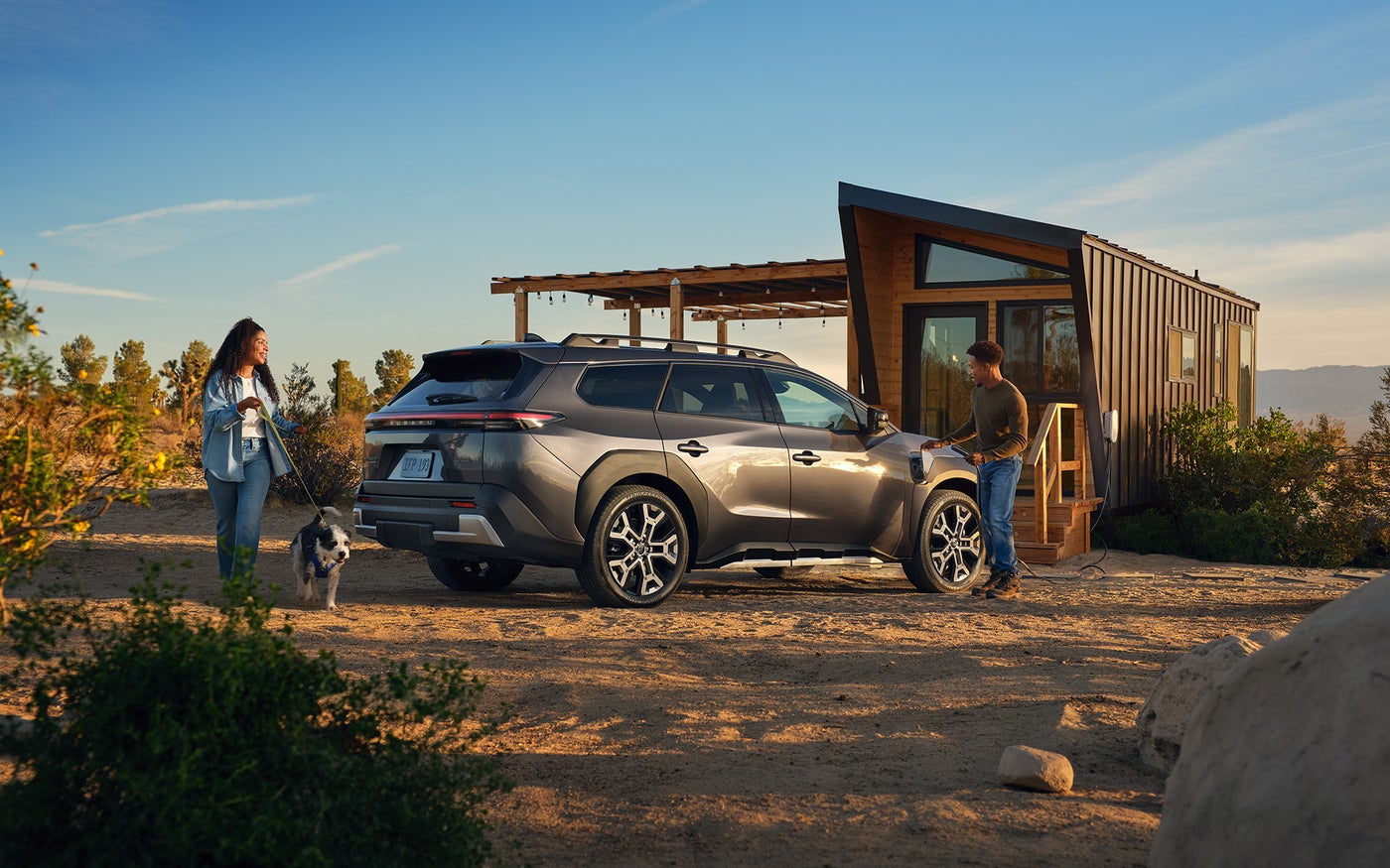 A man charges his Subaru Trailseeker next to a small home.