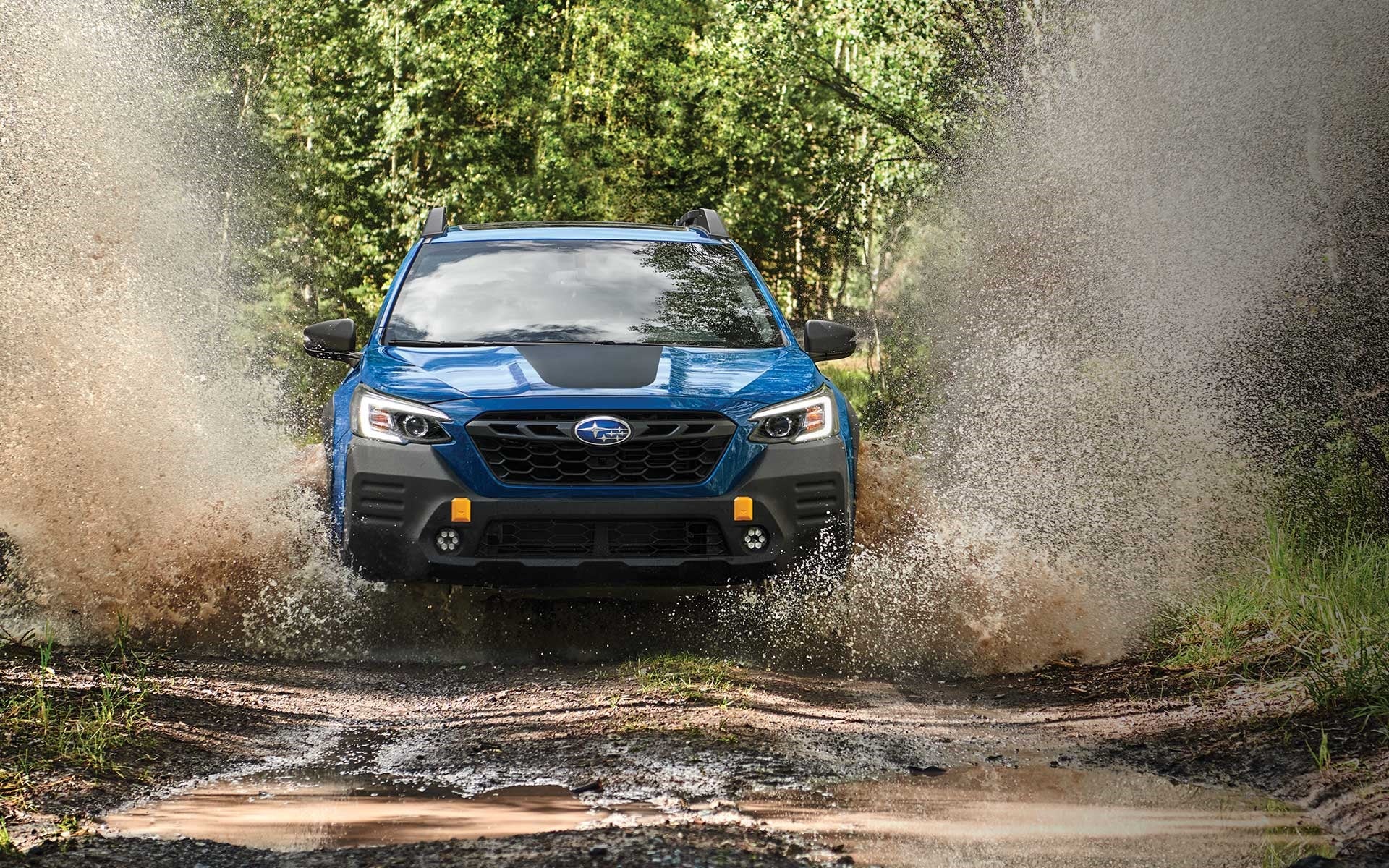 Subaru Outback Wilderness splashing through muddy trail.