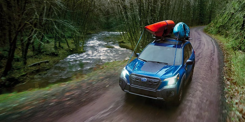 Subaru Forester driving beside a forest river.