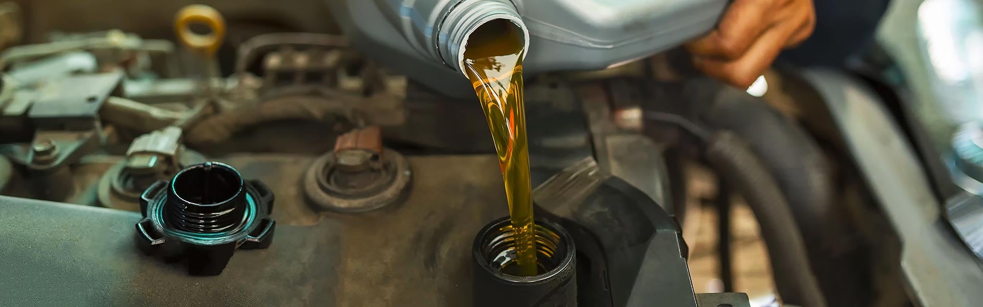 Fresh amber engine oil being poured into a car engine during routine vehicle maintenance.